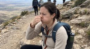 A hiker on a mountain trail pinches her nose to perform the Valsalva maneuver to pop her ears due to altitude pressure.