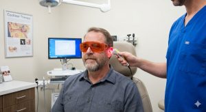 Middle-aged man wearing protective goggles receives low-level laser therapy on his ear in a medical clinic.