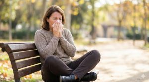 Woman sneezing into a tissue and crossing her legs, illustrating a stress incontinence trigger.