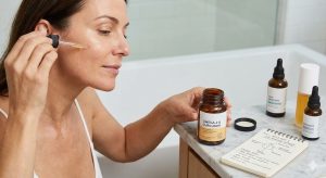 A woman applies facial serum with a dropper, holding a bottle of Omega-3 & Curcumin supplements next to a notebook on PGE2 inhibition and skin health.