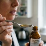 Close-up of a woman taking zinc syrup from a spoon with 5ml dosage bottle.